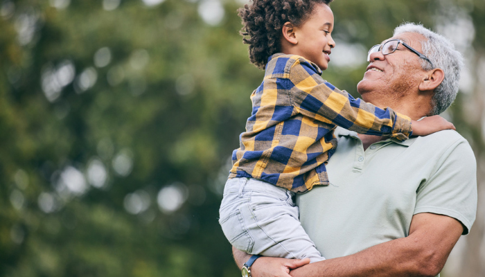 Older grandparent holding young grandson outside smiling