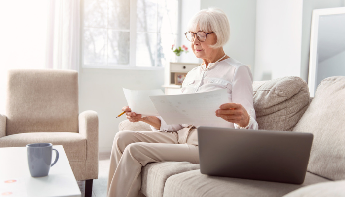 Older woman reading social security paperwork on couch