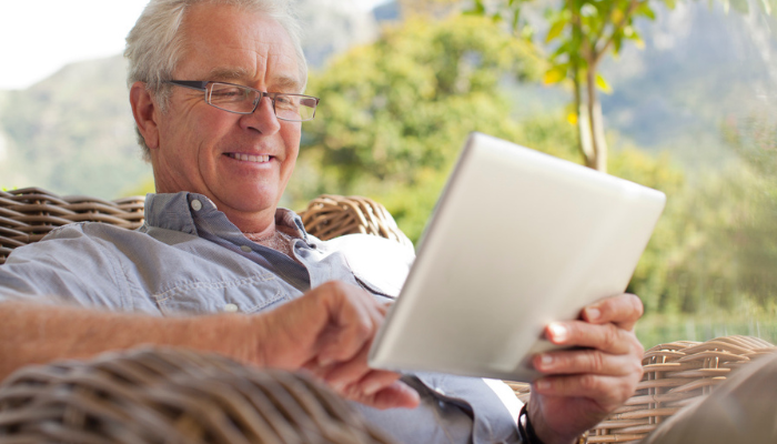 Older man smiling at ebook reader and tablet outside