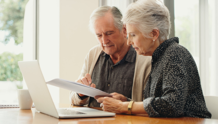 Older couple reviewing documents at laptop together.