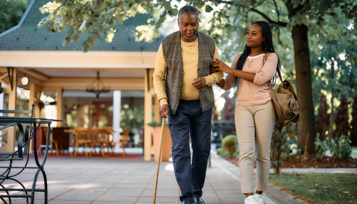 Older man walking outside with a cane with his granddaughter.