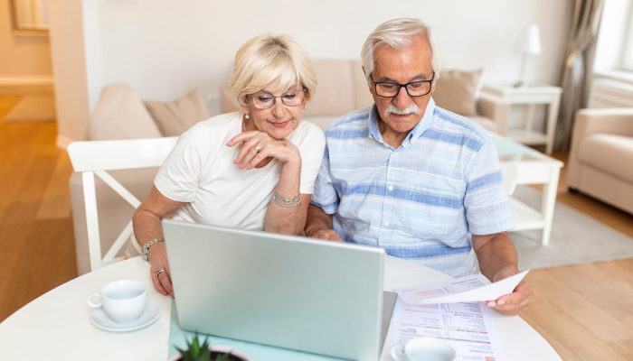 Older couple looking at paperwork and laptop.