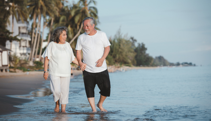 Older Asian couple walking on beach on vacation.
