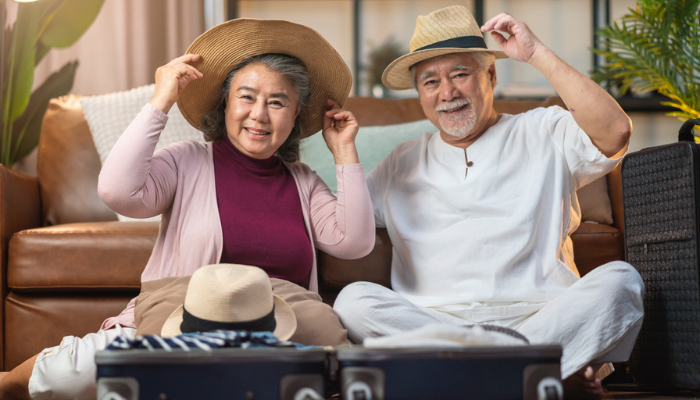 Happy Asian couple trying on hats while packing suitcase