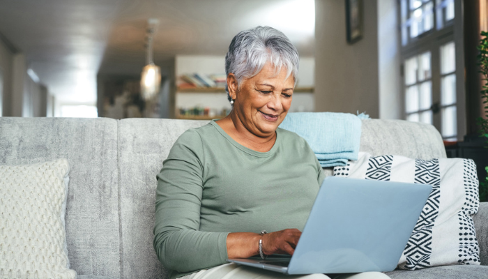 Older woman smiling at laptop on her couch.