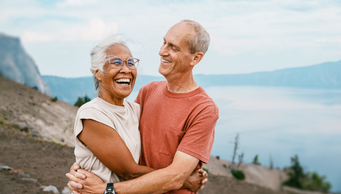 Older senior couple smiling and hugging while hiking.