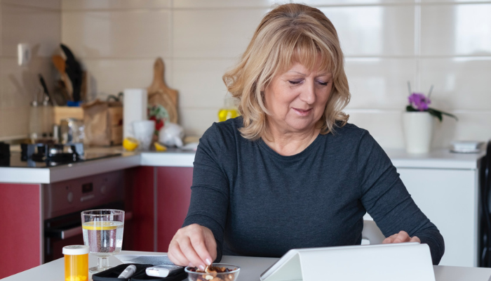 Older woman eating snack in kitchen while on her ipad.
