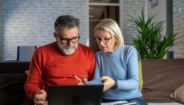 Older man and wife reviewing finances on laptop.