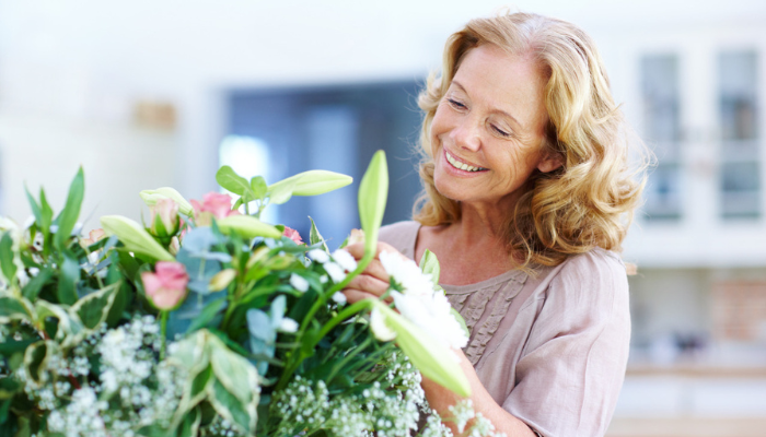 Beautiful senior woman arranging flowers happily at home.
