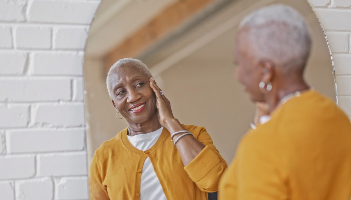 Older African American woman admiring skin in mirror.