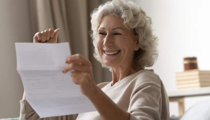 Older woman smiling reading paperwork.
