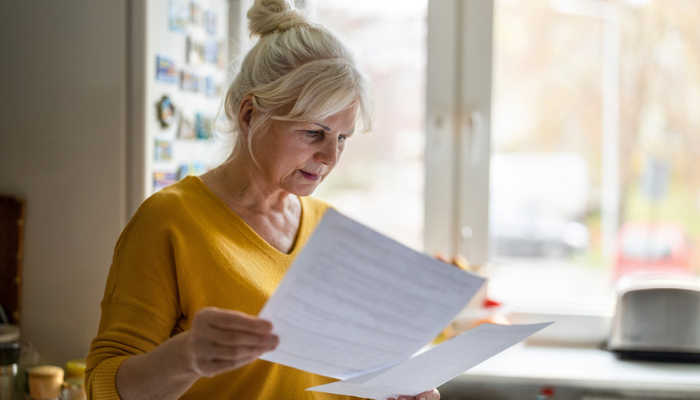 Older woman in yellow shirt reading Medicare paperwork.