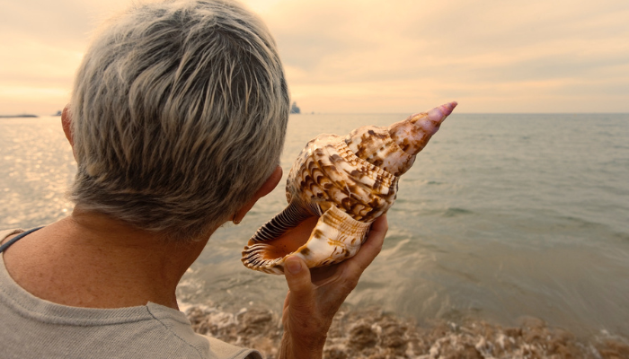 Senior man listening to shell at the beach.