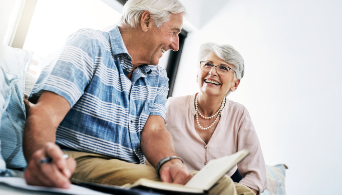 Senior couple smiling writing in journal together.