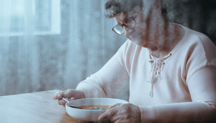 Senior woman eating bowl of soup.