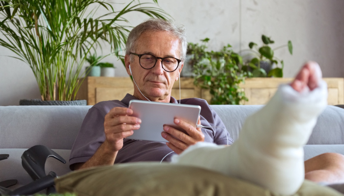 Senior man on iPad with leg in cast.