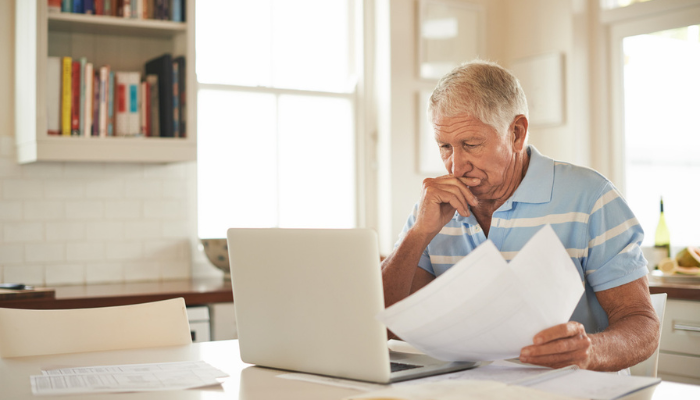 Older man reviewing paperwork and laptop.