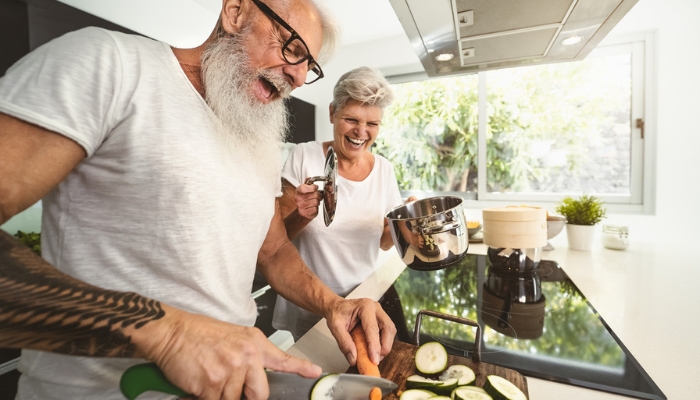 Happy vegan and vegetarian older couple cooking in kitchen at home.