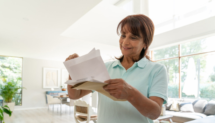 Happy older woman opening mail at home.