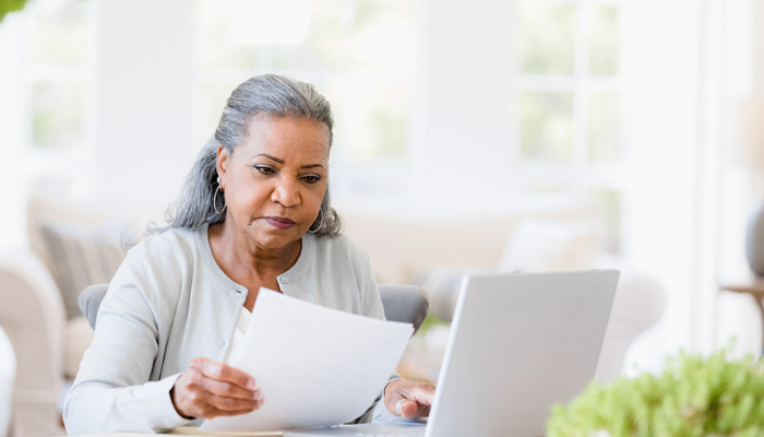Older African American woman reading bill and laptop in home.