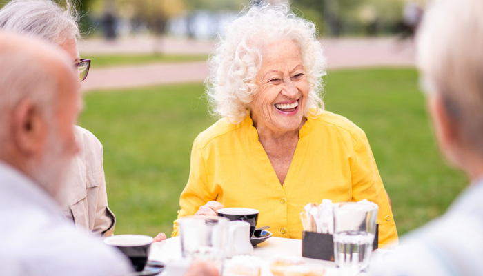 Happy older woman laughing wearing yellow shirt outside with friends.
